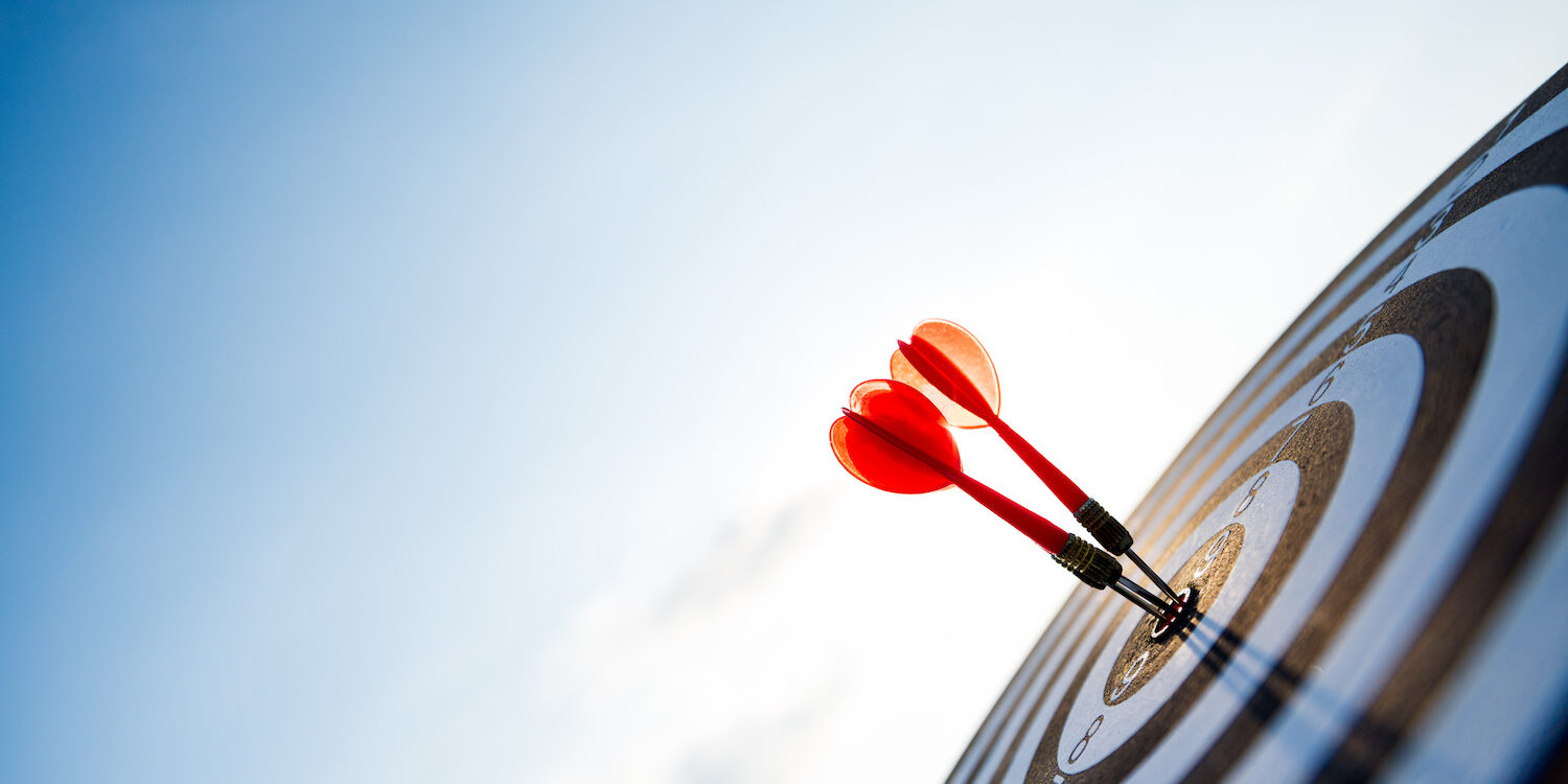 Close up shot red darts arrows in the target center on dark blue sky background. Business target or goal success and winner concept.